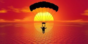 Silhouette of a paraglider flying over the ocean towards a crimson sunset